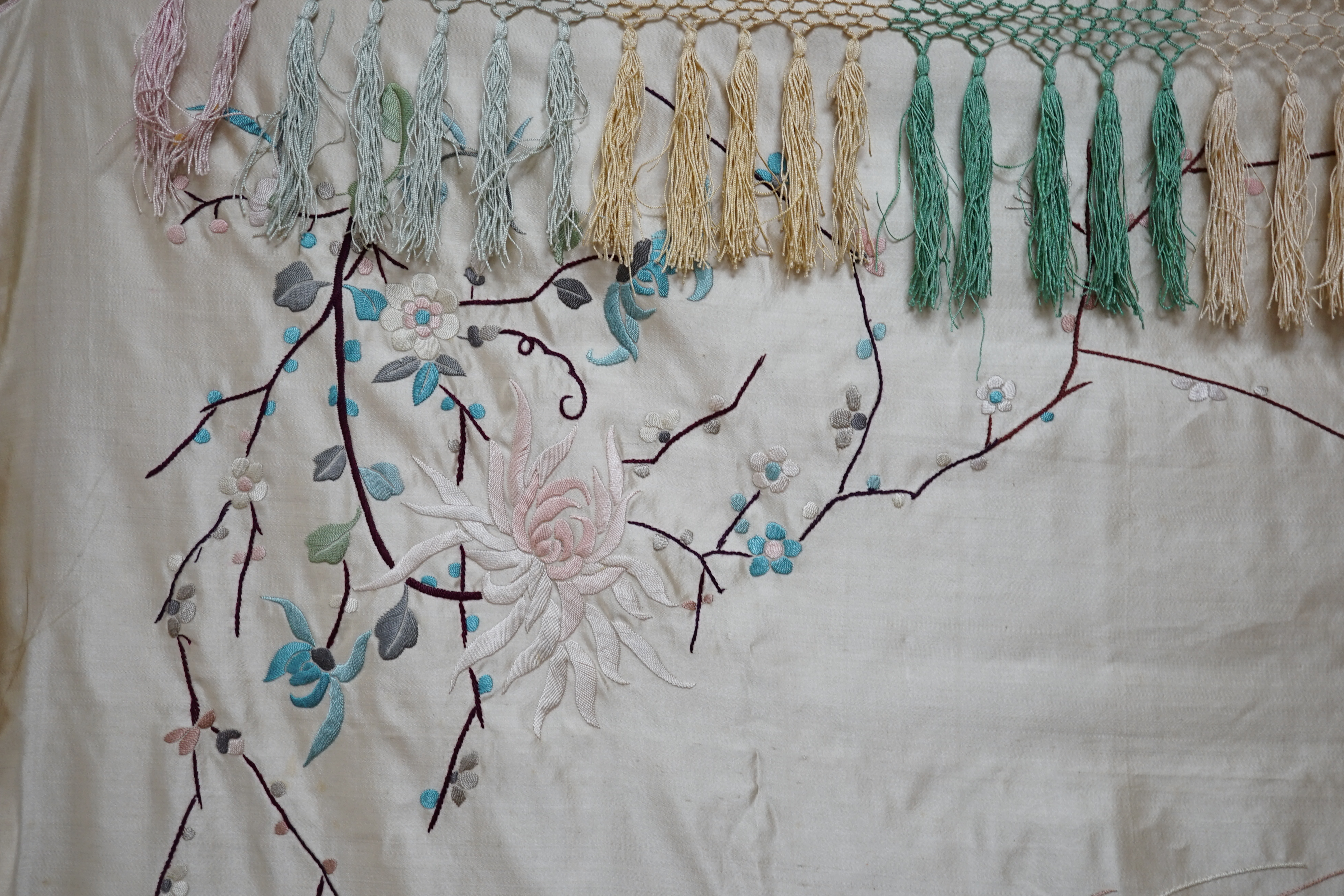 A 1920’s-30’s Chinese oyster silk satin embroidered shawl, now converted to a wall hanging, embroidered in pastel coloured silk threads, the large central motif of two dragons playing with a pearl, the corners of the han